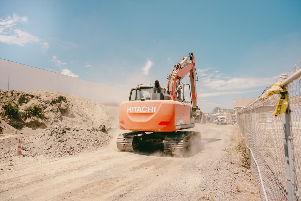 Excavator tracking across the yard with dust rolling behind it